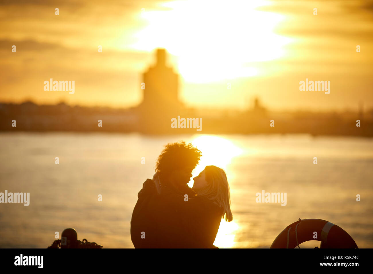 Pier Head Liverpool Waterfront mit Blick über den Fluss Mersey in Birkenhead bei Sonnenuntergang ein junges Paar kiss Stockfoto