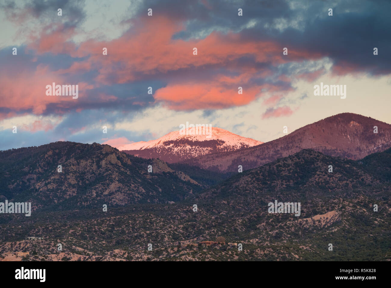 Dramatischer Sonnenuntergang und Wolken über die schneebedeckten Gipfel von Santa Fe Baldy über eine Nachbarschaft in Tesuque, in der Nähe von Santa Fe, New Mexico Stockfoto