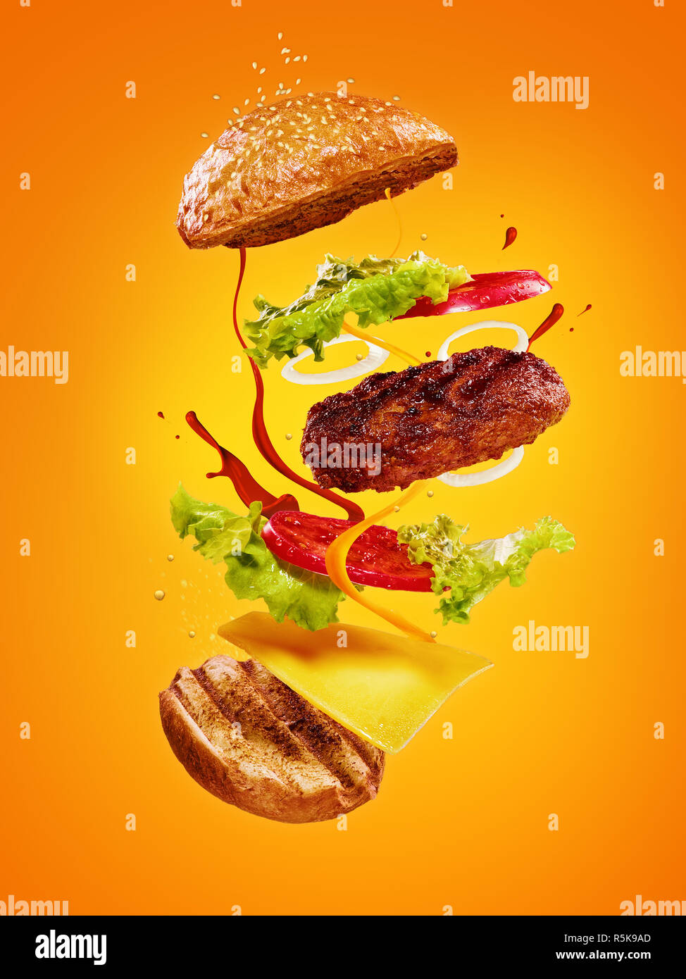 Die Hamburger mit fliegenden Zutaten auf orangefarbenem Hintergrund Stockfoto