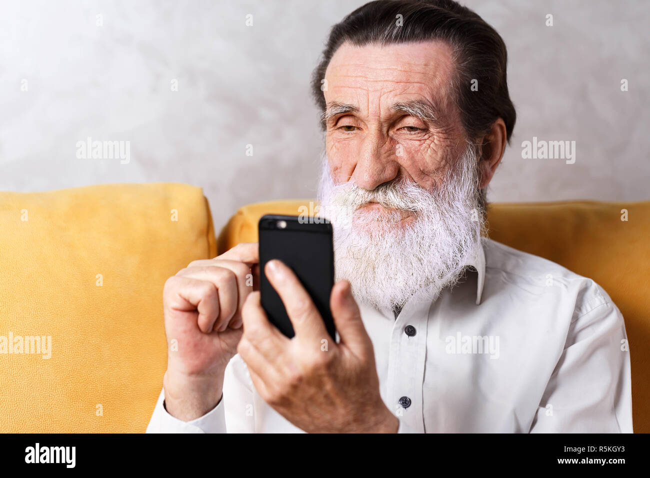 Stattlichen älteren bärtigen Mann mit weißem T-Shirt gelb sitzen auf dem Sofa und schreiben Nachricht Stockfoto