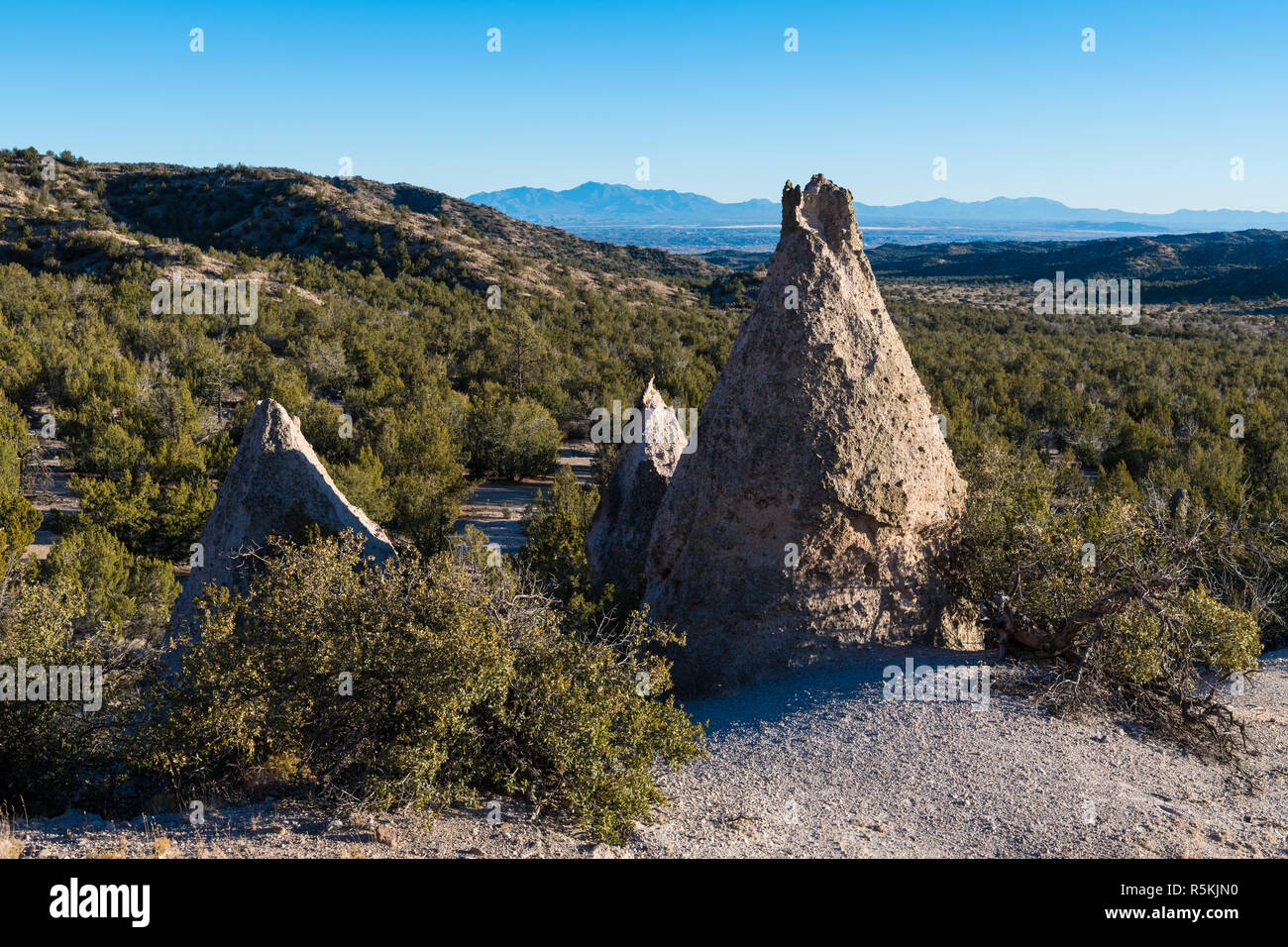 Eine Gruppe von drei ungewöhnliche, konisch geformten Felsen im Kasha-Katuwe Tent Rocks National Monument mit Sicht auf das Tal und die Berge Stockfoto