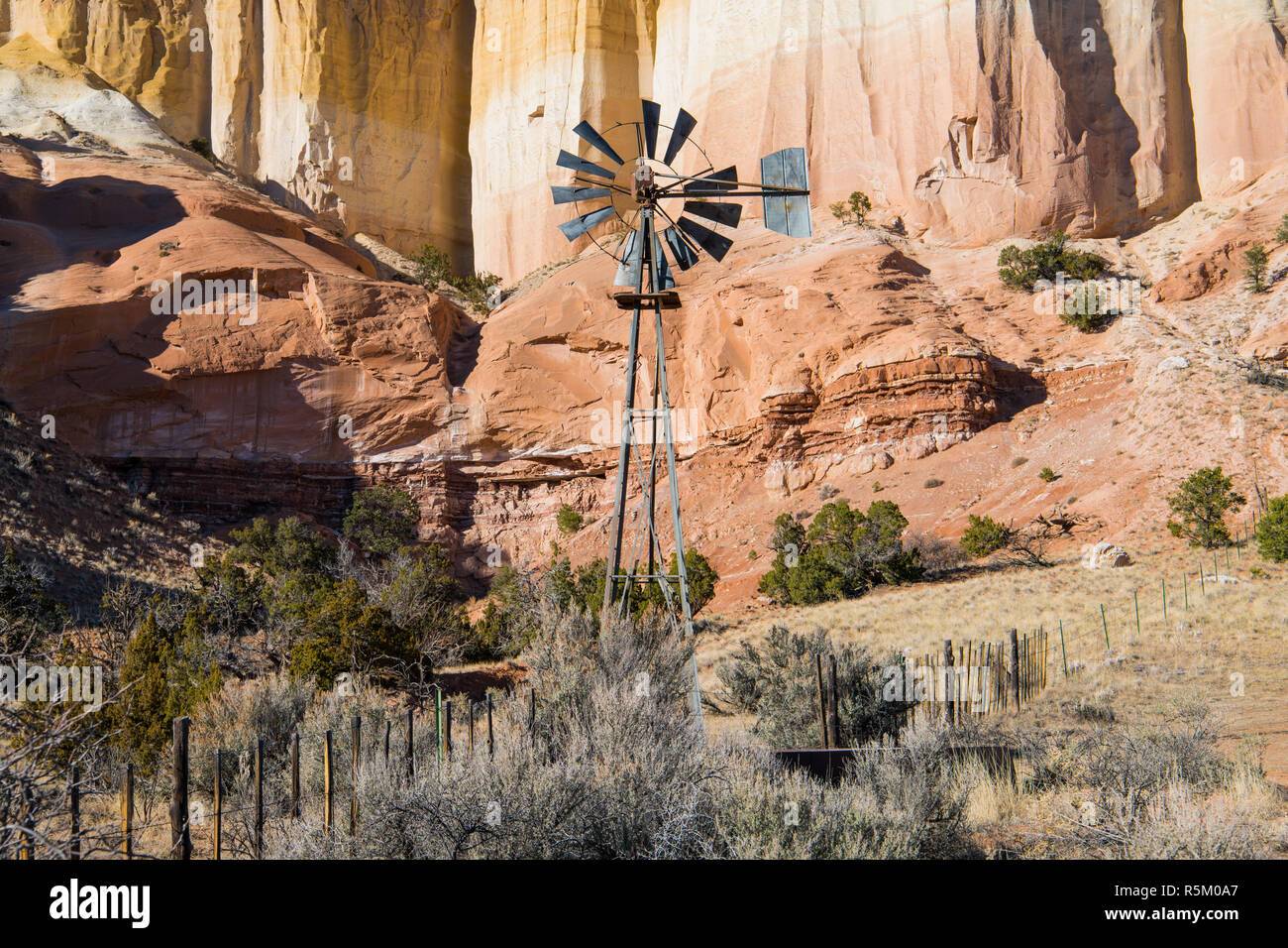 Old Ranch Windmühle und Zaun vor der bunten hohen Klippen in der Wüste Landschaft des nördlichen New Mexico Stockfoto