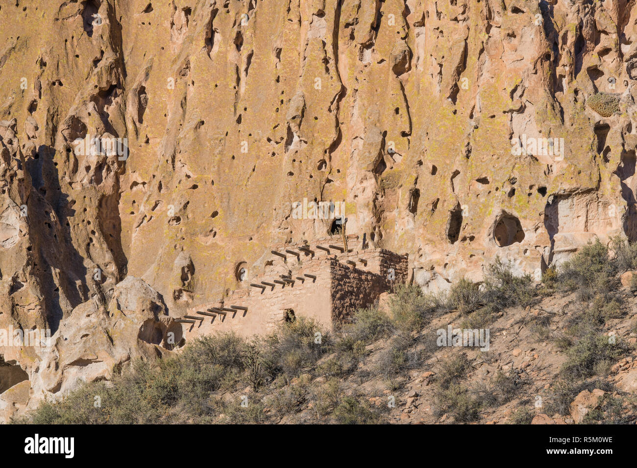 Alte adobe Ruinen entlang der Basis des bunten Felsen am Bandelier National Monument, New Mexico Stockfoto