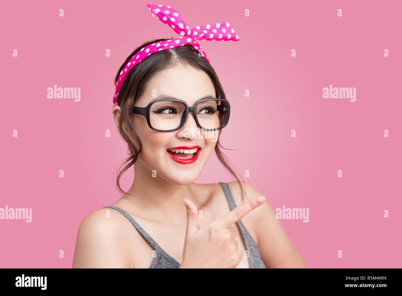 Portrait von asiatischen Mädchen mit hübsch Lächeln in pinup Style zeigt auf rosa Hintergrund Stockfoto