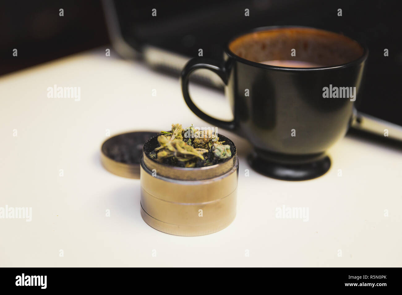 Cannabis oder Marihuana Blume in einem Stahl Schleifer auf einen Schreibtisch, neben einer Tasse Kaffee und einem Laptop. Stockfoto