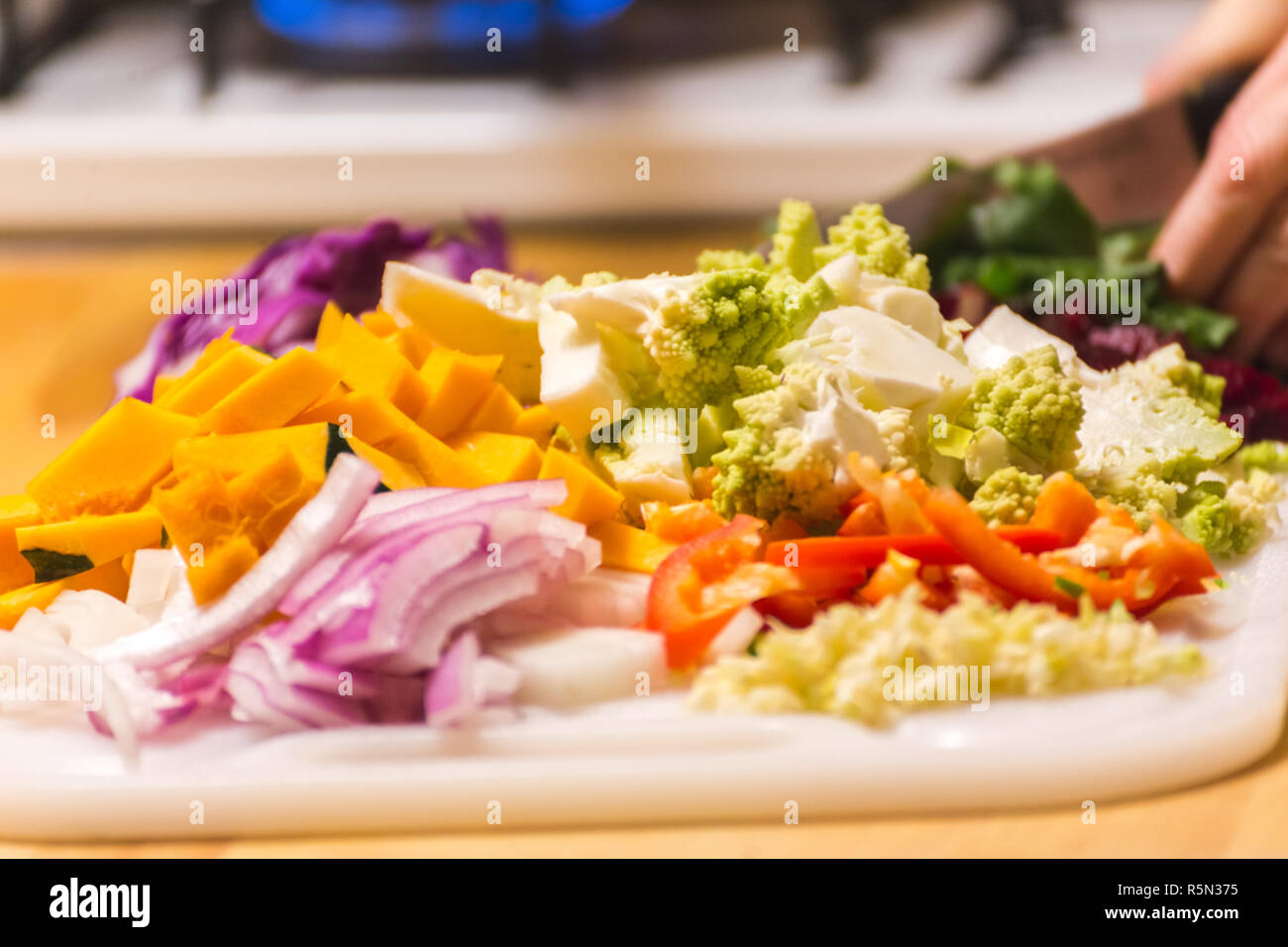 Stapel von gehacktes Gemüse auf einer hölzernen Schneidebrett oder hackklotz. Gemüse gehören Squash, Zwiebeln, Paprika, Brokkoli und Romanesco. Stockfoto