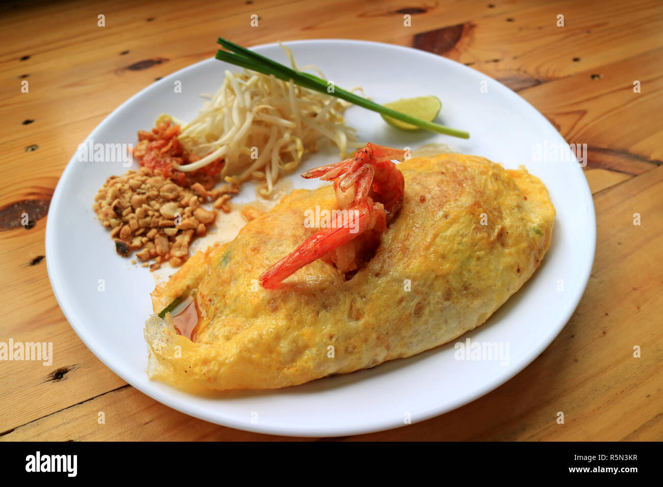 Thai gebratene Nudel- oder Pad Thai eingewickelt in Spiegelei überbacken mit Garnelen serviert auf hölzernen Tisch Stockfoto