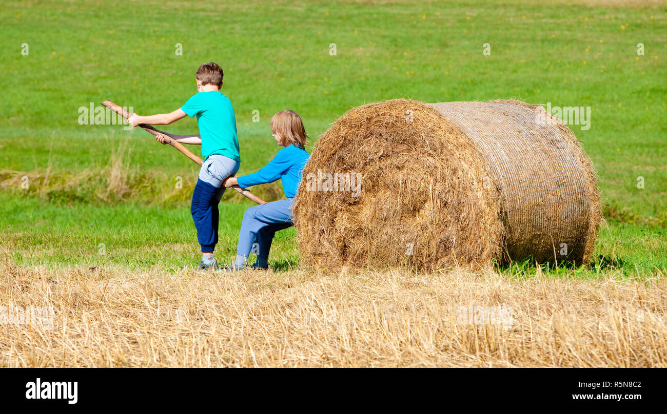 Zwei jungen, die Ballen Heu mit Stick als Hebel bewegen Stockfoto