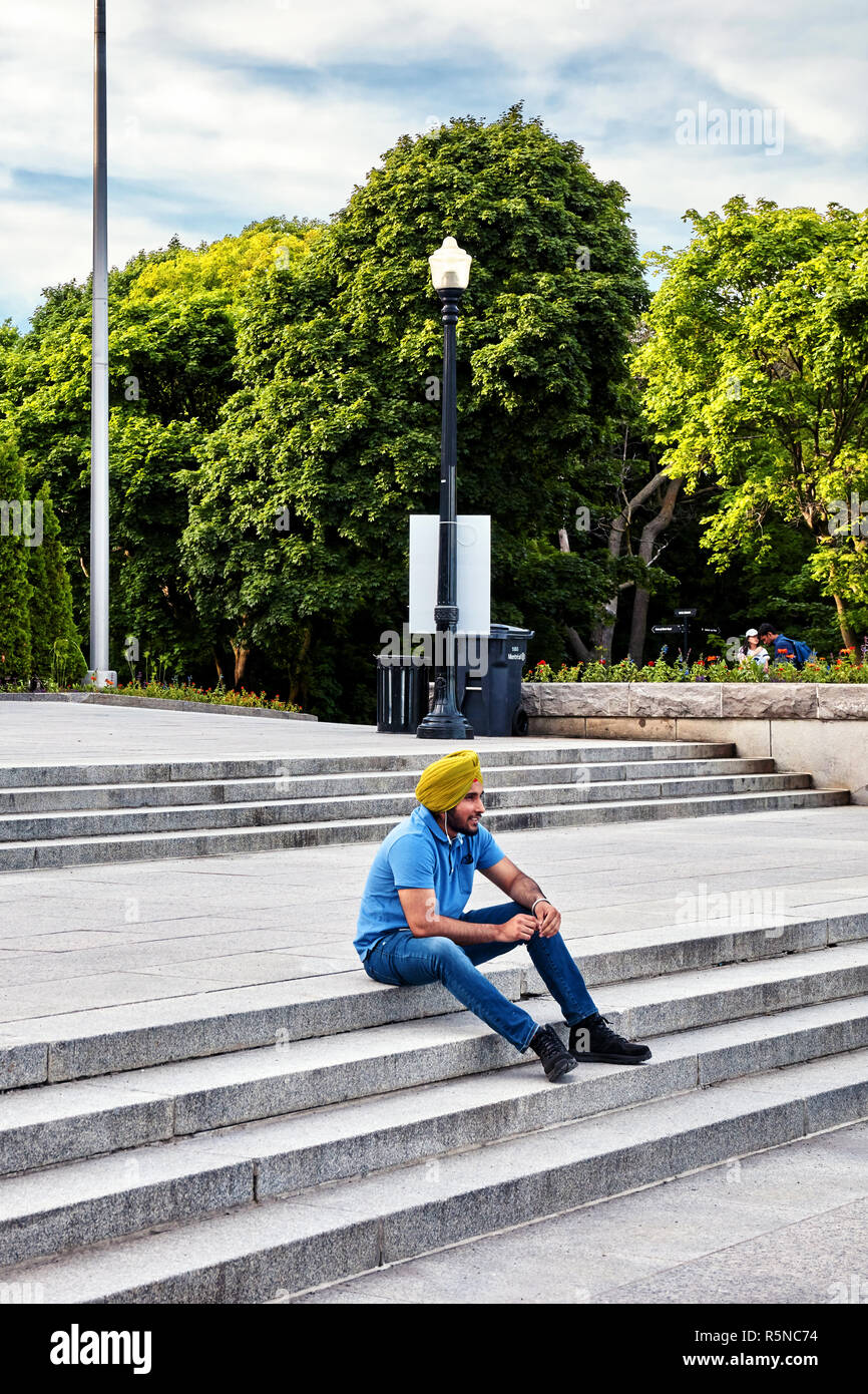 Junge indische Sikh sitzen auf der Treppe des Mount Royal Park und ein Gespräch mit seinen Kopfhörern in Montreal, Kanada. Stockfoto