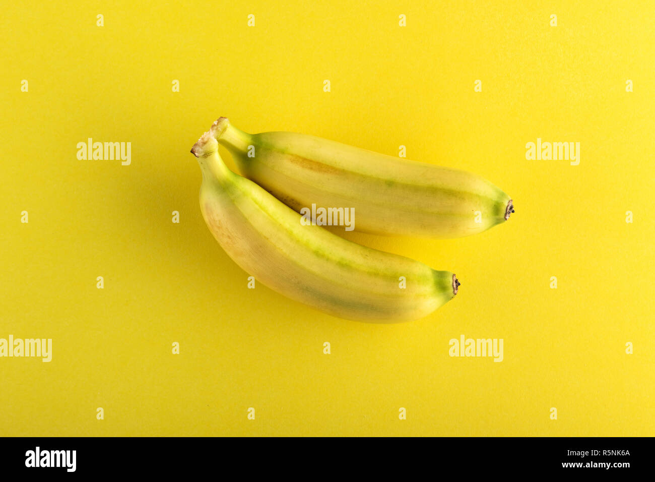 Zwei kleine ganze Bananen von oben gesehen auf gelbem Hintergrund Stockfoto