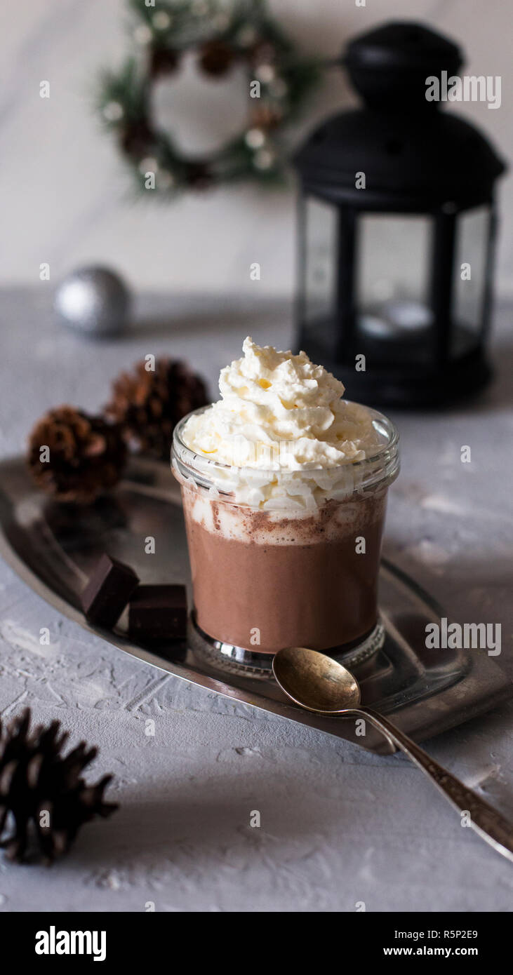 Heiße Schokolade im Glas auf Metall Fach mit Löffel und schwarz Laterne in der Nähe auf grauen Hintergrund. Weihnachten Komposition. Stockfoto