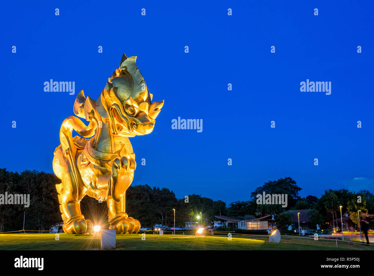 CHIANG RAI, THAILAND - OCT. 27 2016: Gold Singha Statue an Singha Park ist das Symbol von Boon Rawd Farm im Rampenlicht während der Dämmerung auf blauen Himmel Hintergrund umgeben, berühmte touristische Destination, OCT. 27 2016 in Thailand. Stockfoto