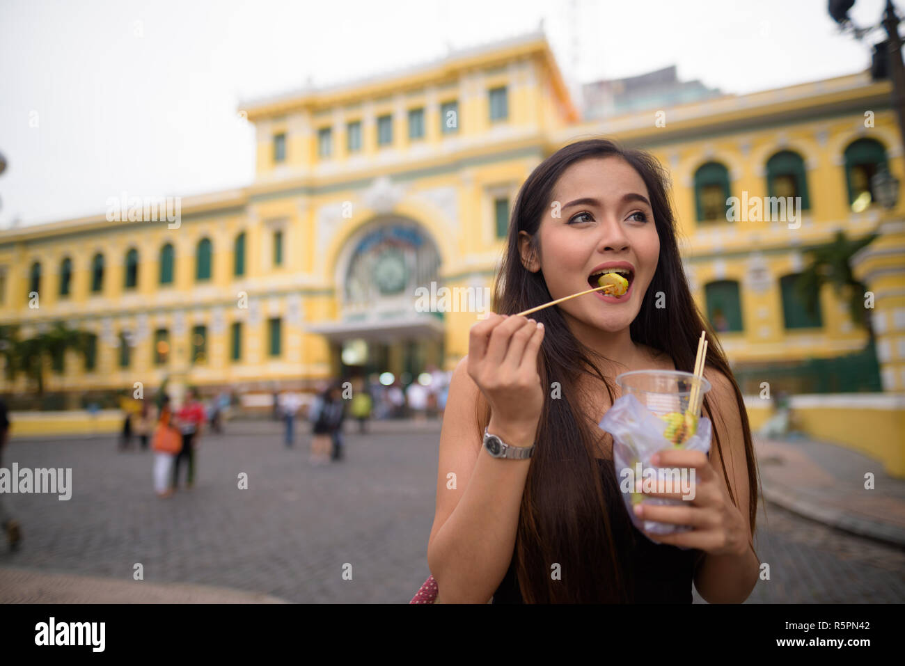 Asiatische Frau Essen vor Saigon Central Post Office Stockfoto