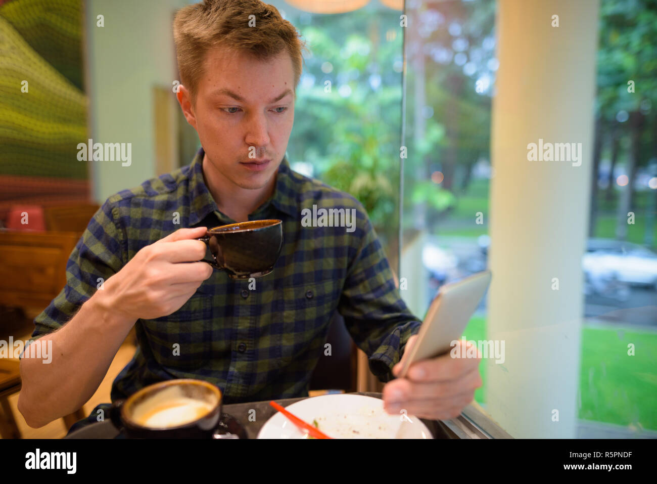 Mann sitzt im Restaurant Kaffee trinken, während mit Handy Stockfoto