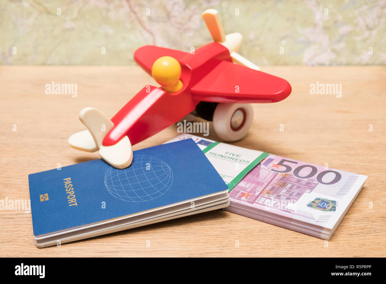 Biometrischer Reisepass, ein Flugzeug und ein Bündel von euro Geld liegen auf einem Holztisch auf dem Hintergrund einer unscharfen Karte Stockfoto