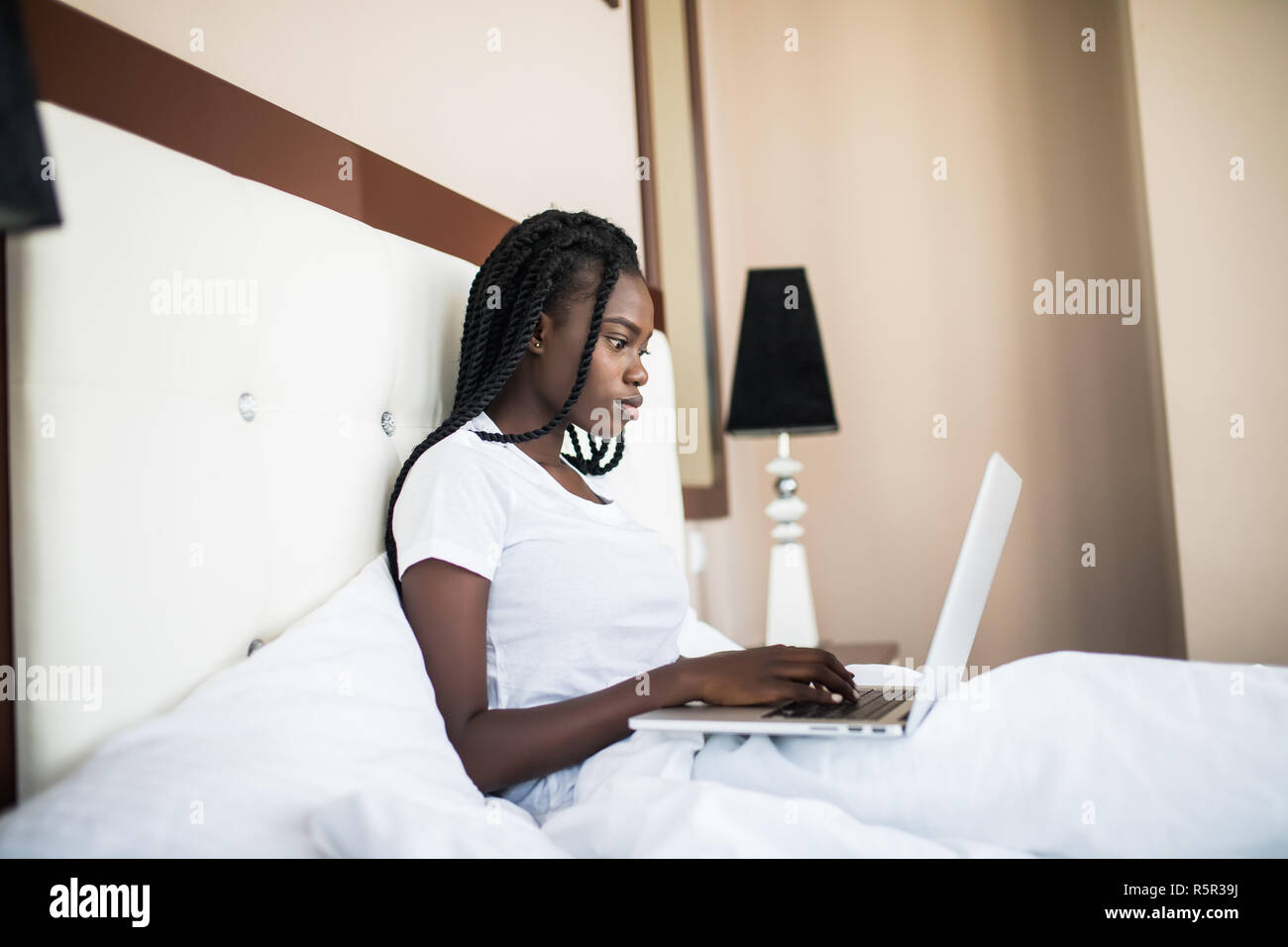 Portrait von Afrikanische amerikanische Frau zu Hause Schlafzimmer sitzen fröhlich auf dem Bett Vernetzung über Laptop lächelnd Internet genießen. Stockfoto