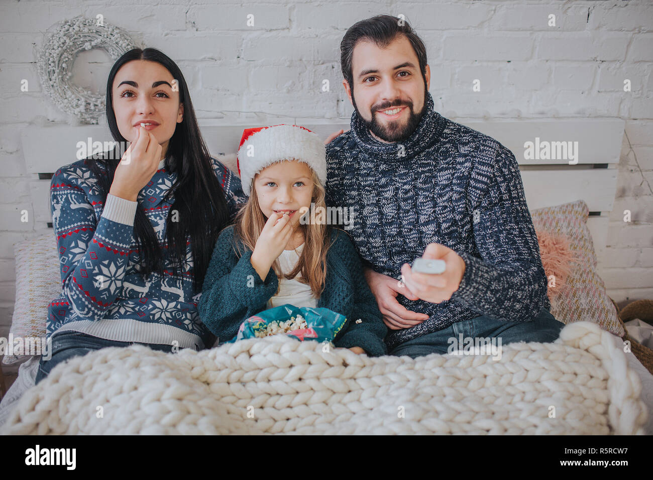 Frohe Weihnachten und guten Rutsch ins neue Jahr. Junge Familie Urlaub zu Hause feiern. Der Vater ist, halten Sie die Fernbedienung vom Fernseher. Vater, Tochter und Mutter sind Fernsehen. Stockfoto