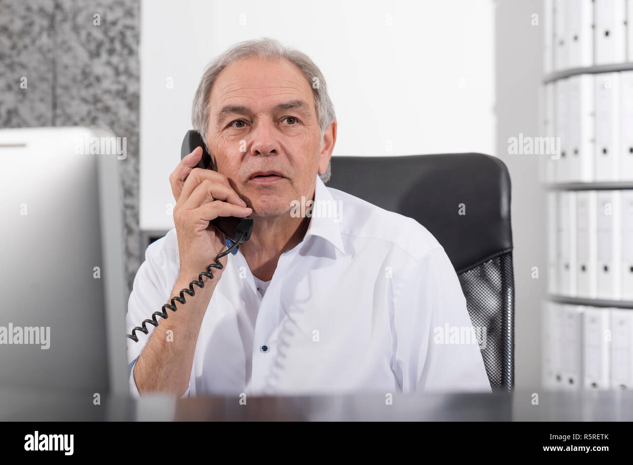 Älterer Mann mit weißem Hemd an einem Schreibtisch sitzen Stockfoto
