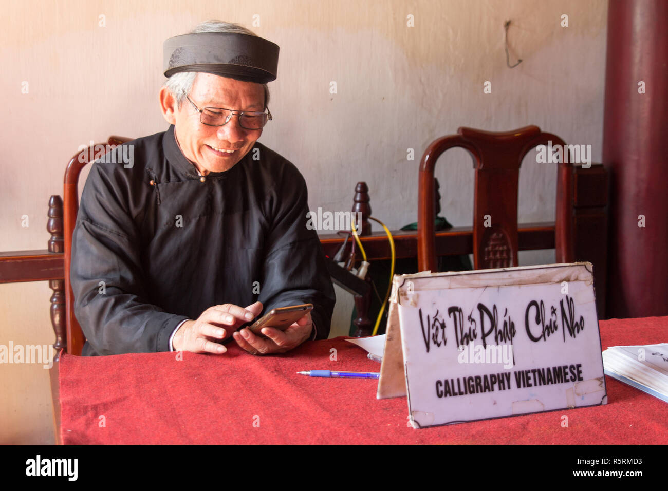 Hanoi, Vietnam - ca. Oktober 2015: kalligraph in Hanoi, Vietnam bietet seine Dienstleistungen und Handy zugleich. Stockfoto