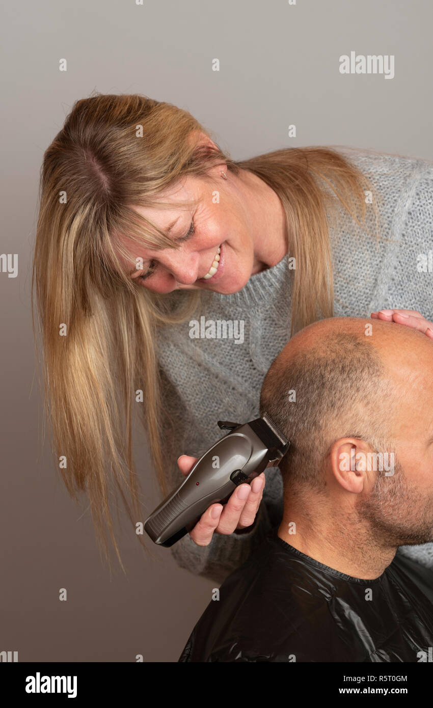 Frau mit tragbaren elektrischen Haarschneidemaschinen ein balding Mann einen Bürstenschnitt Frisur. Stockfoto