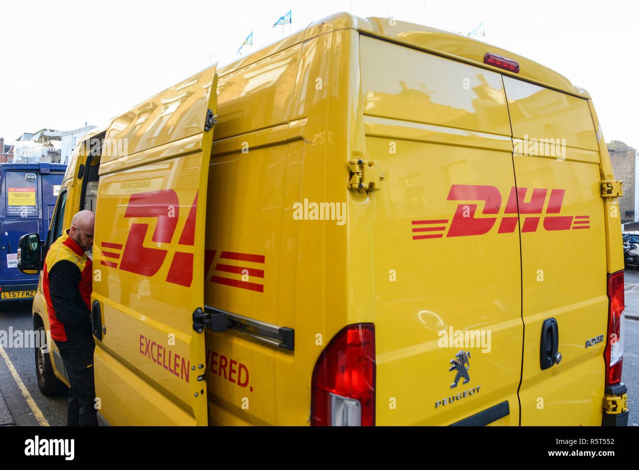 Nahaufnahme des gelben DHL-Lieferwagens und des Fahrers beim Entladen von Paketen Stockfoto