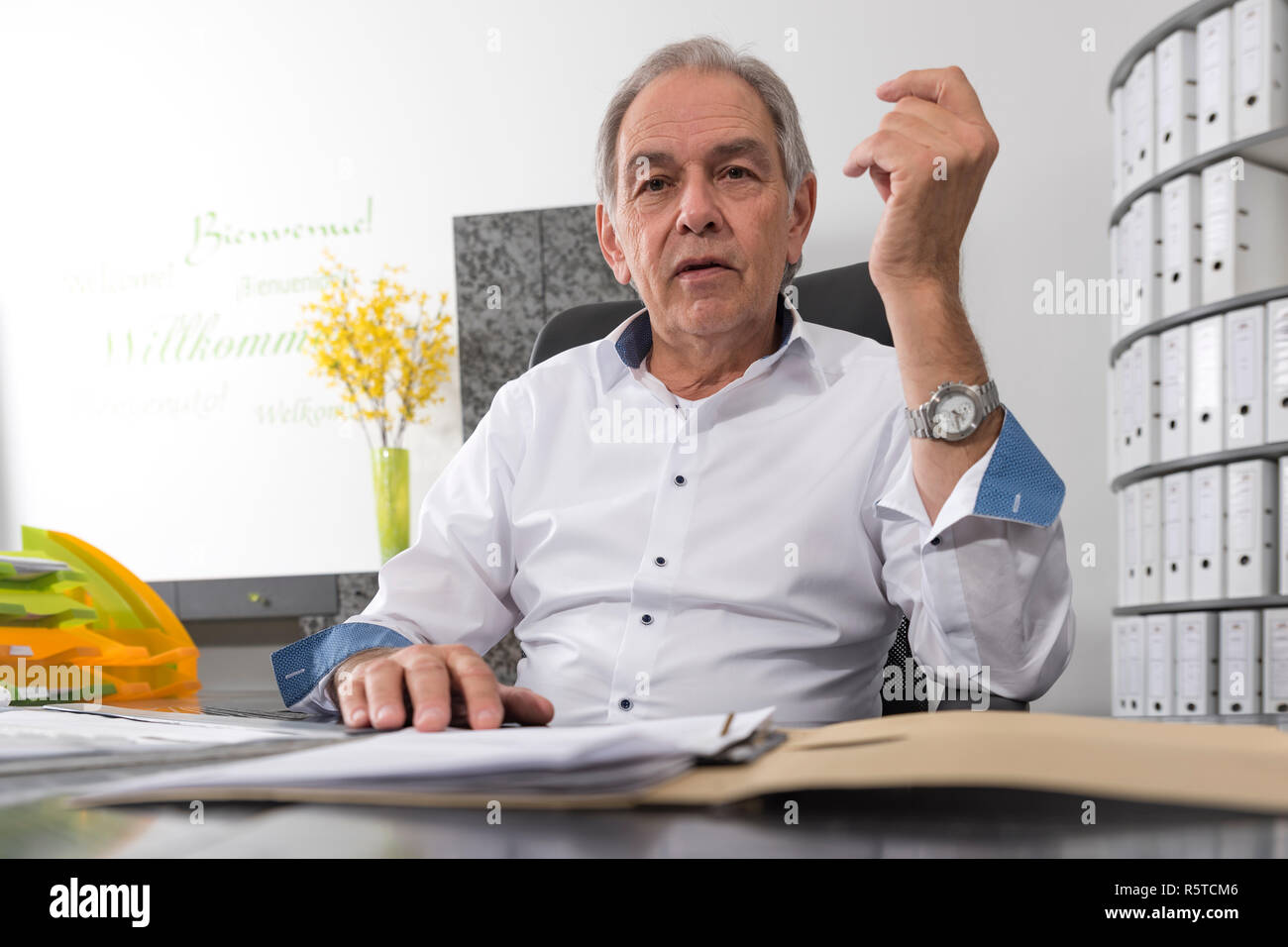 Älterer Mann mit weißem Hemd sitzt an einem Schreibtisch Stockfoto
