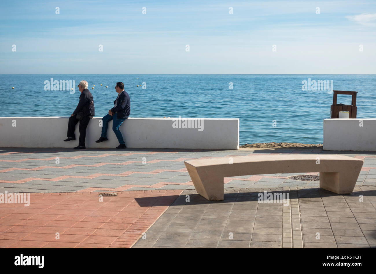 Zwei ältere Männer an der Strandpromenade sitzend, mit modernen öffentlichen Bank vor, La Cala, Andalusien, Spanien. Stockfoto