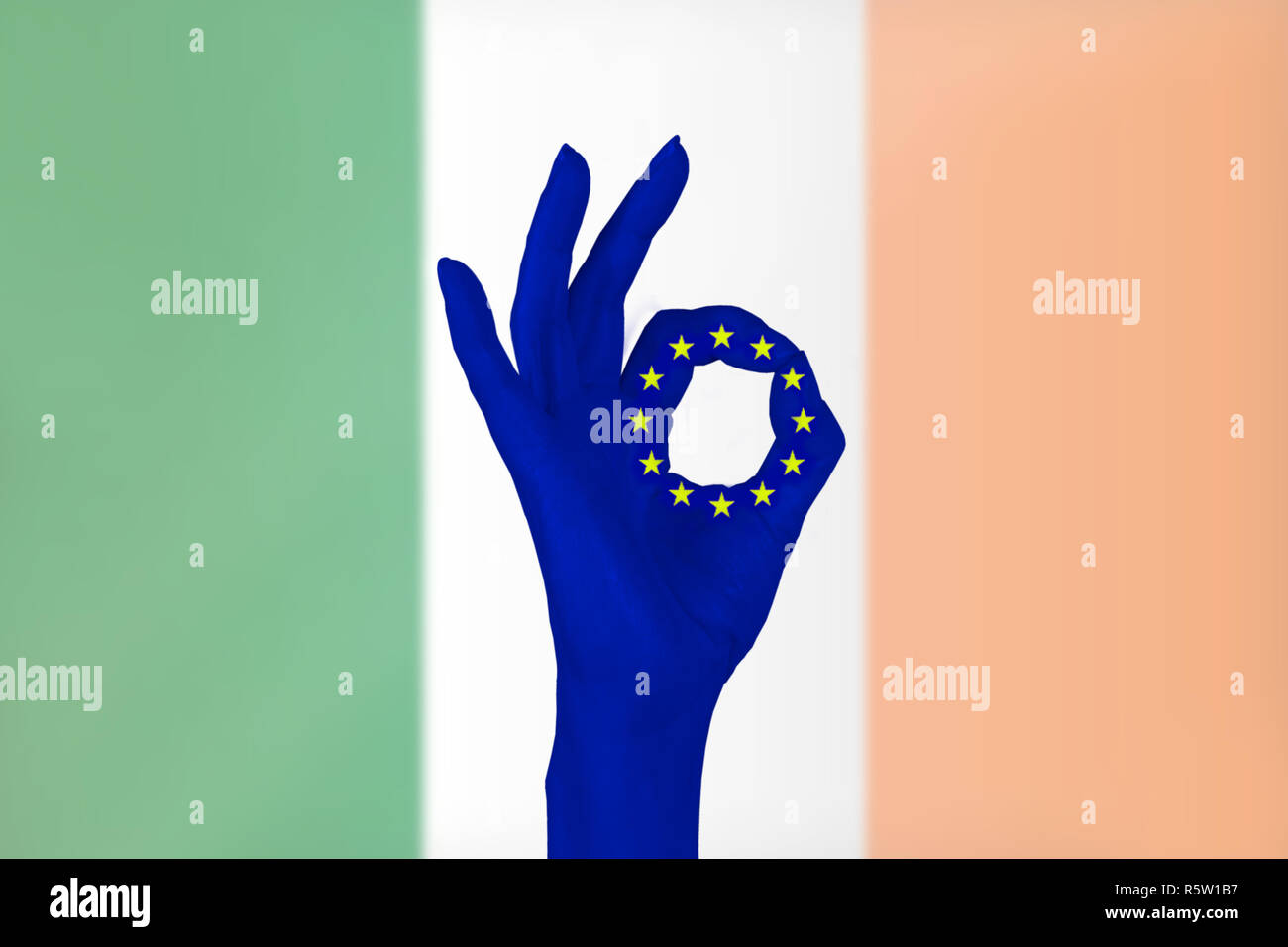 Ein erhobenen Hand macht das OK-Zeichen. Zwischen Daumen und Zeigefinger sehen wir das Symbol der Europäischen Union. Die irische Flagge im Hintergrund. Stockfoto