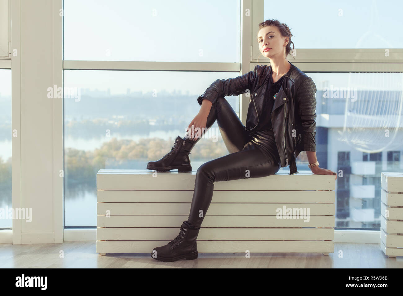 Schöne junge Frau in schwarzem Leder Anzug saß am Fenster. Stockfoto