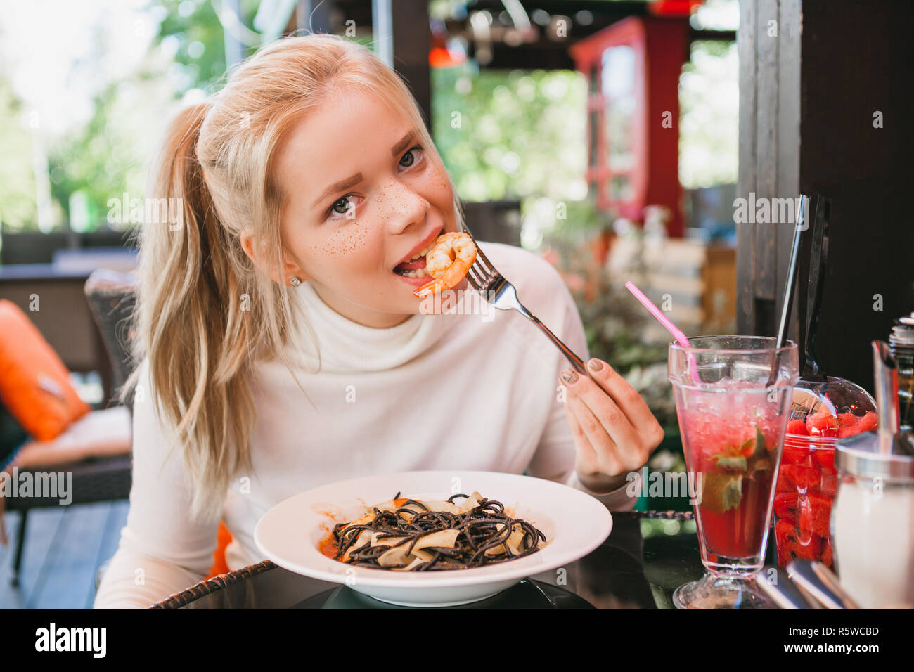 Junge schöne Frau essen schwarze Nudeln mit Meeresfrüchten und Tintenfisch Tinte in das Restaurant im Freien. Lustig und schön. Stockfoto