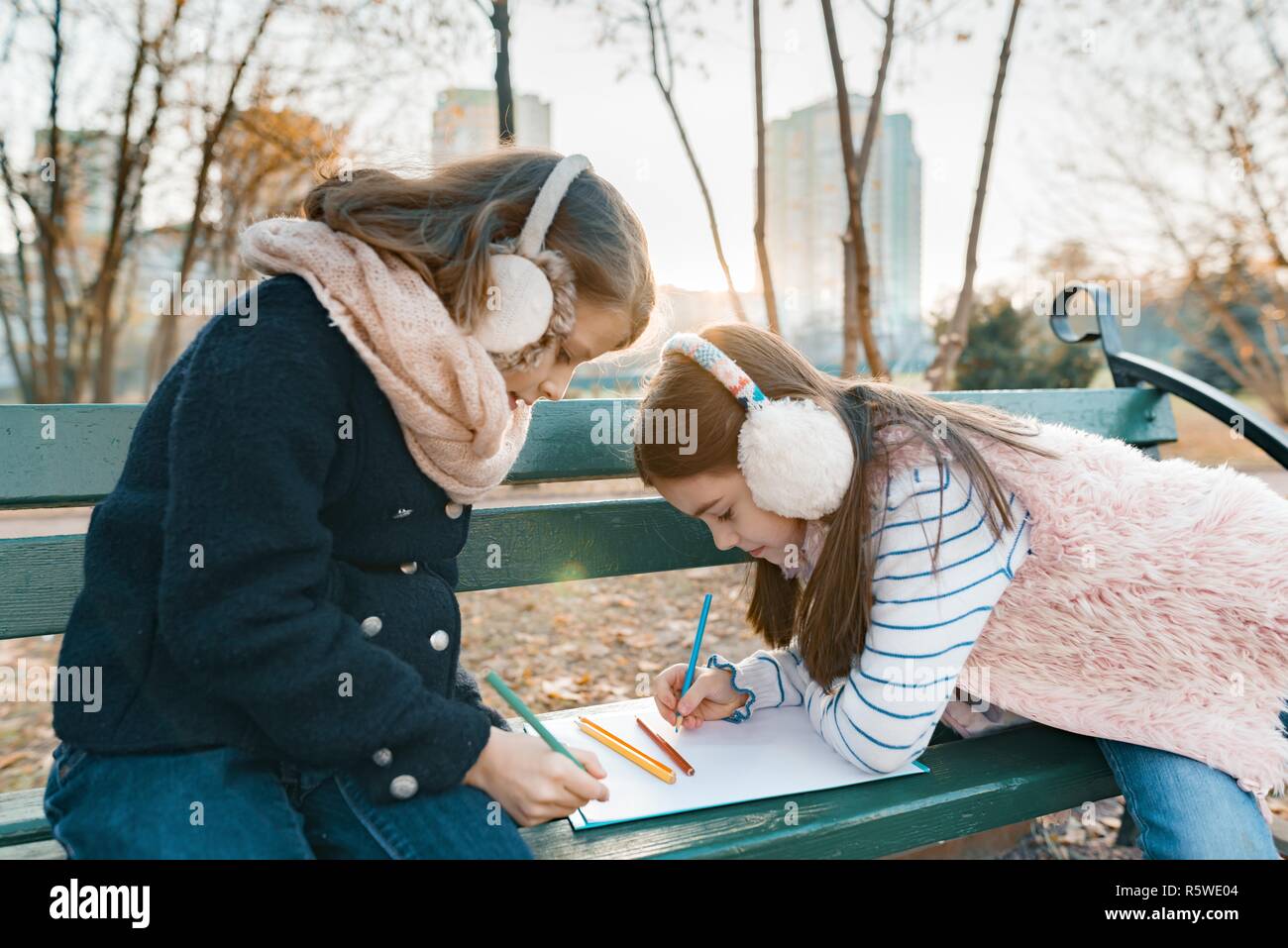 Zwei kleine hübsche Künstler Zeichnen mit Farbstiften, Mädchen sitzen auf einer Bank im sonnigen Herbst Park, goldenen Stunde. Stockfoto