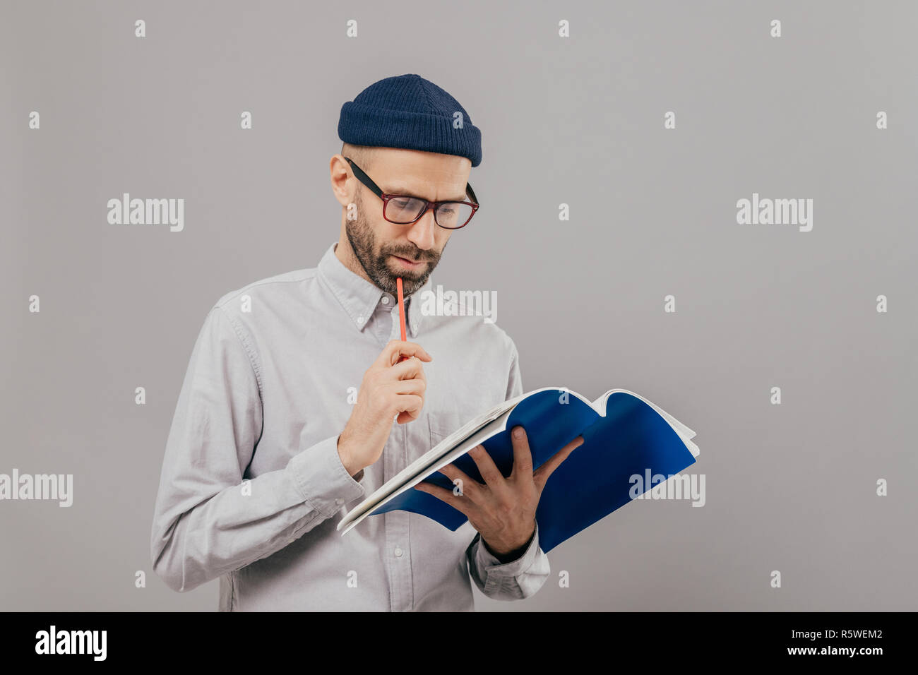 Konzentriert unrasierten Mann Stift hält, Schaut aufmerksam in geöffnete Buch, lernt neue Informationen, bereitet sich für Seminar, trägt formelle Kleidung, isolierte ov Stockfoto