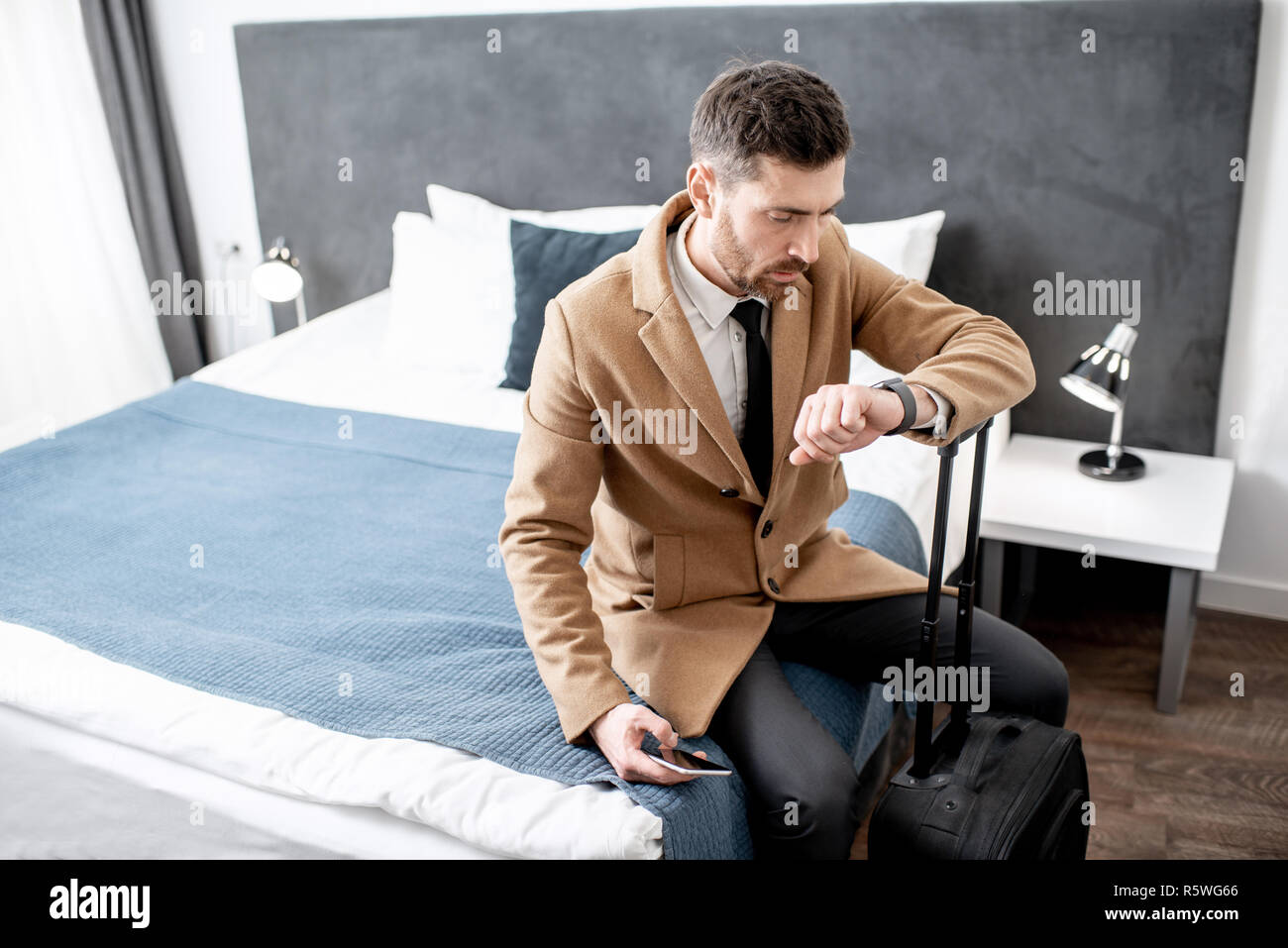 Gekleidete Geschäftsmann auf dem Bett mit einem Koffer gerade Zeit sitzen vor der Abreise aus dem Hotel Zimmer Stockfoto