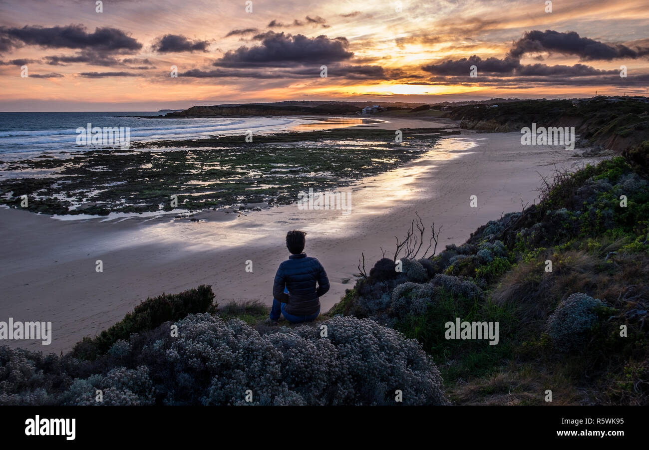 Eine Frau in den späten 20s beobachtet den Sonnenuntergang am Strand zurück, Torquay in Australien Stockfoto