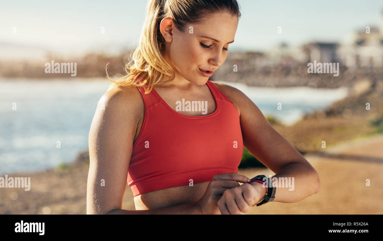 Läuferin eine Pause von Ihrem Workout mit Blick auf ihre Armbanduhr. Sportlerin einstellen ihre Uhr steht in der Nähe der Küste. Stockfoto