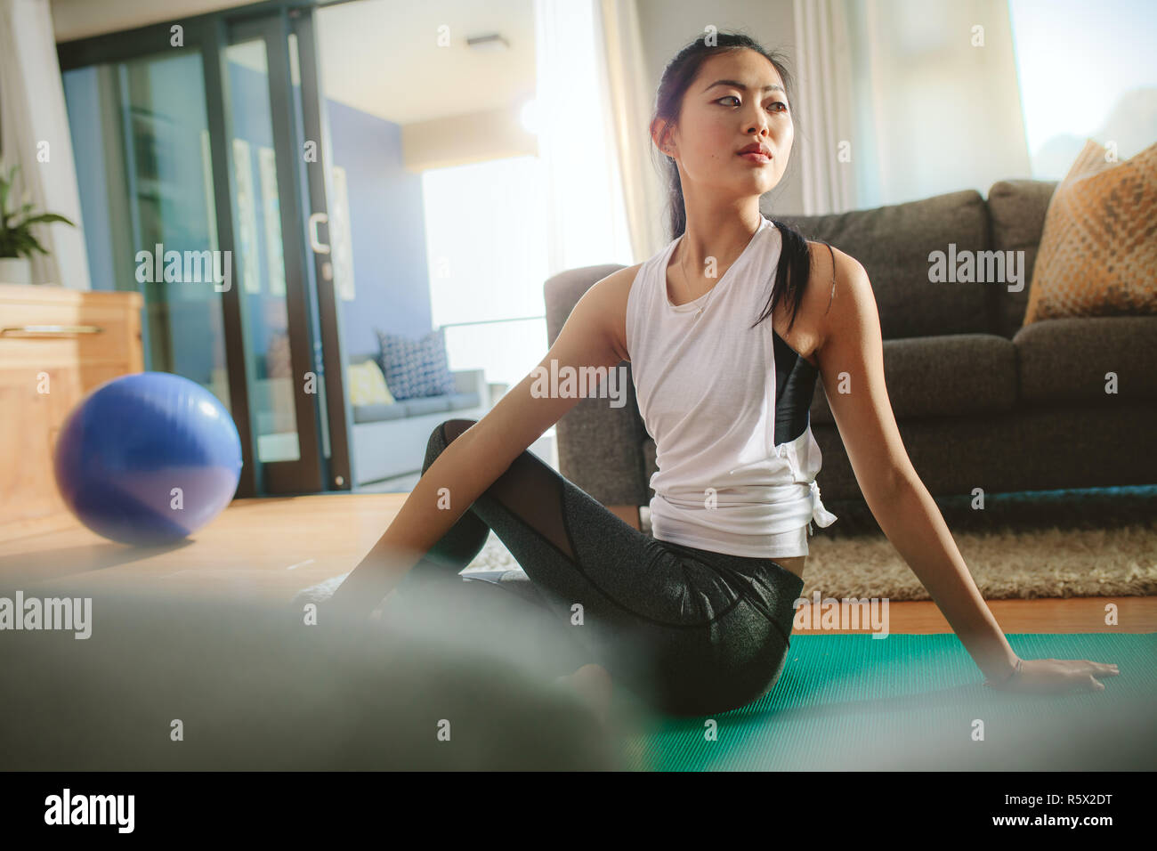 Junge chinesische Frau Yoga Übung zu Hause. Weibliche in Sportkleidung sitzen auf trainingsmatte und drehen ihre Körper. Stockfoto