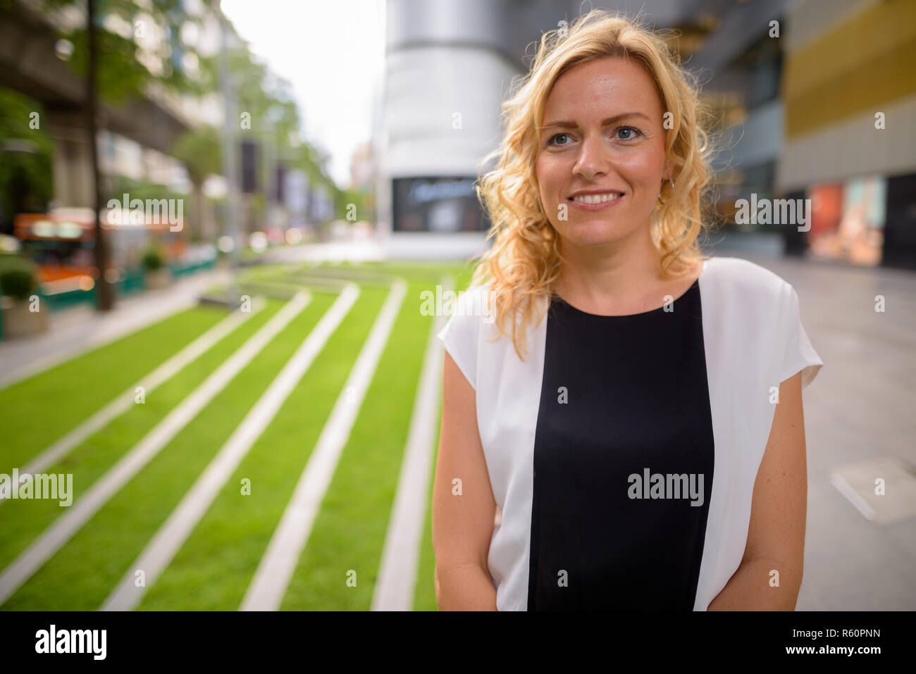 Porträt der schönen blonden Geschäftsfrau, lächeln und denken im Freien Stockfoto
