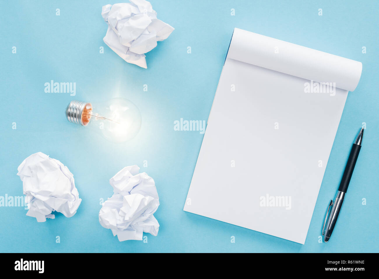 Blick von oben auf die leere Notebook mit zerbröckelt Papier Kugeln und leuchtende Glühbirne auf blauem Hintergrund, in neue Ideen Konzept Stockfoto