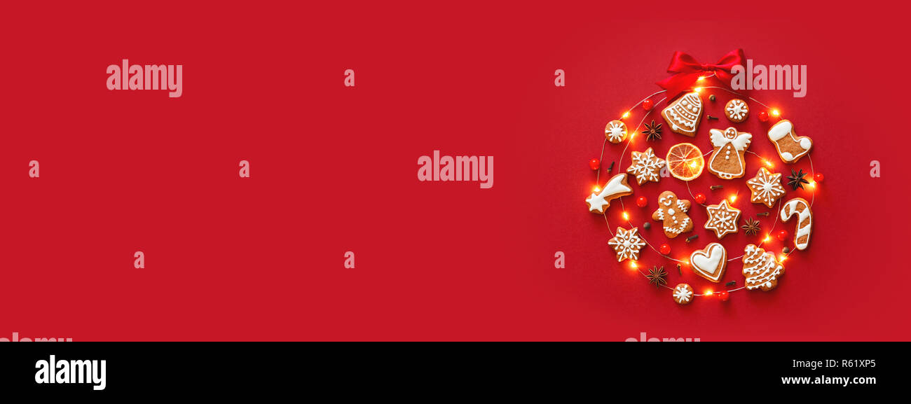 Creative Christmas Ball aus iced Lebkuchen cookies, Anis Sterne, Beeren, orange Chips, dekoriert mit roten Schleife auf rotem Hintergrund. Neues Jahr Banner. Ansicht von oben. Stockfoto
