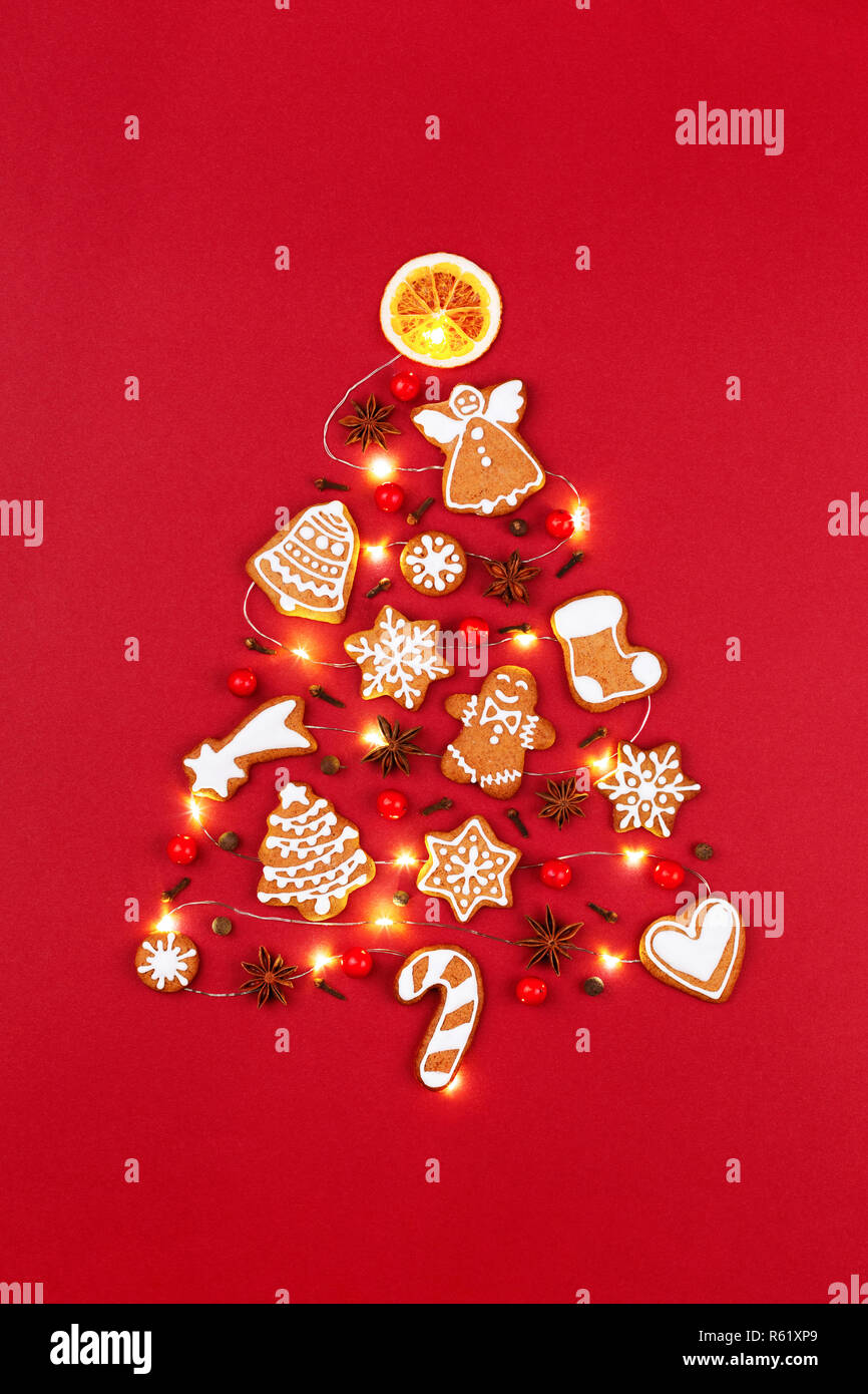 Kreative Weihnachtsbaum aus iced Lebkuchen cookies, Anis Sterne, Beeren, orange Chips, dekoriert mit roten Schleife auf rotem Hintergrund. Neues Jahr Grußkarten-Konzept. Ansicht von oben. Stockfoto