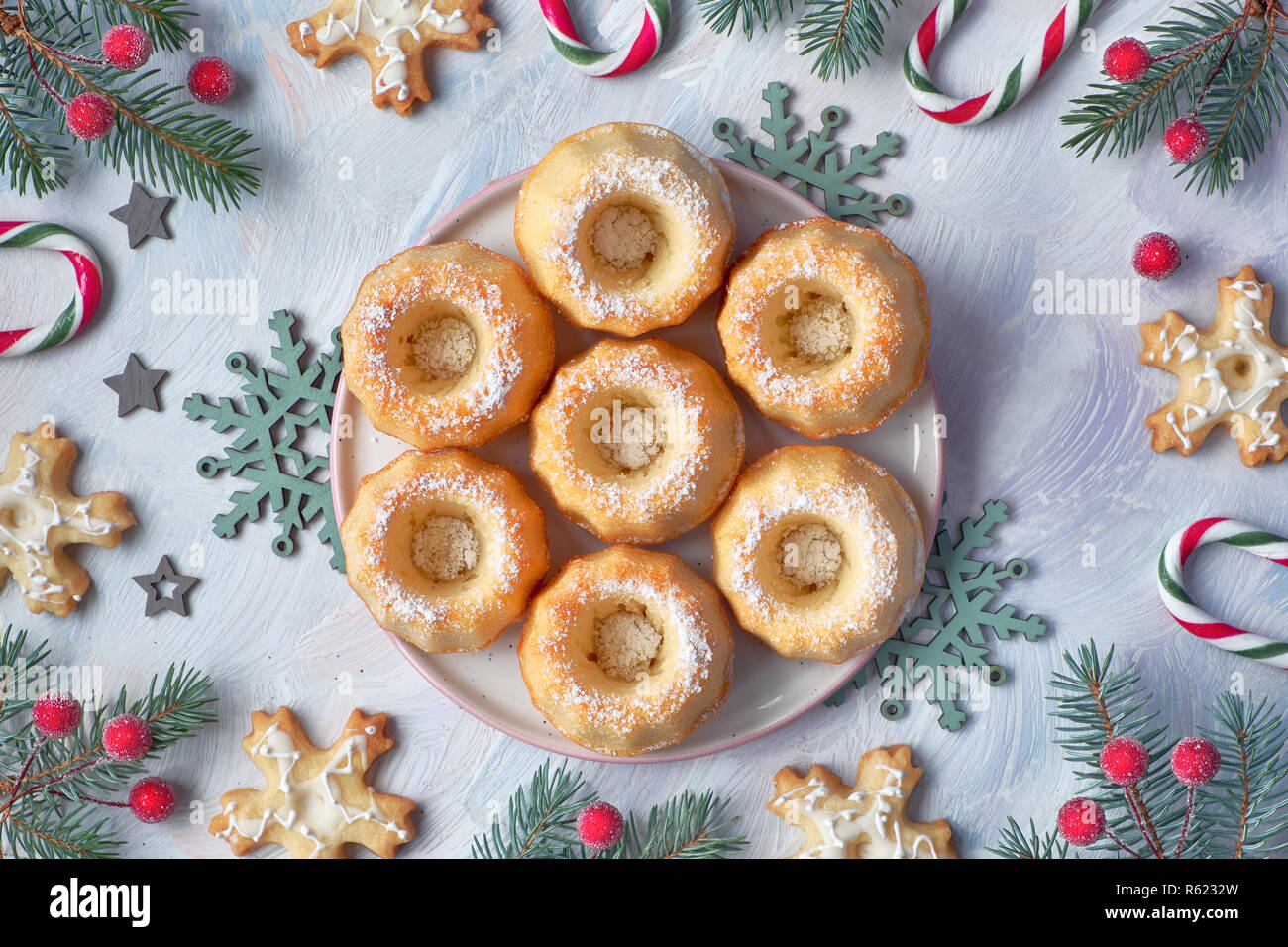 Mini bundt ring Kuchen mit Puderzucker auf hellen Hintergrund mit fir Zweige, Beeren und Zuckerstangen. Weihnachten süße Speisen. Stockfoto