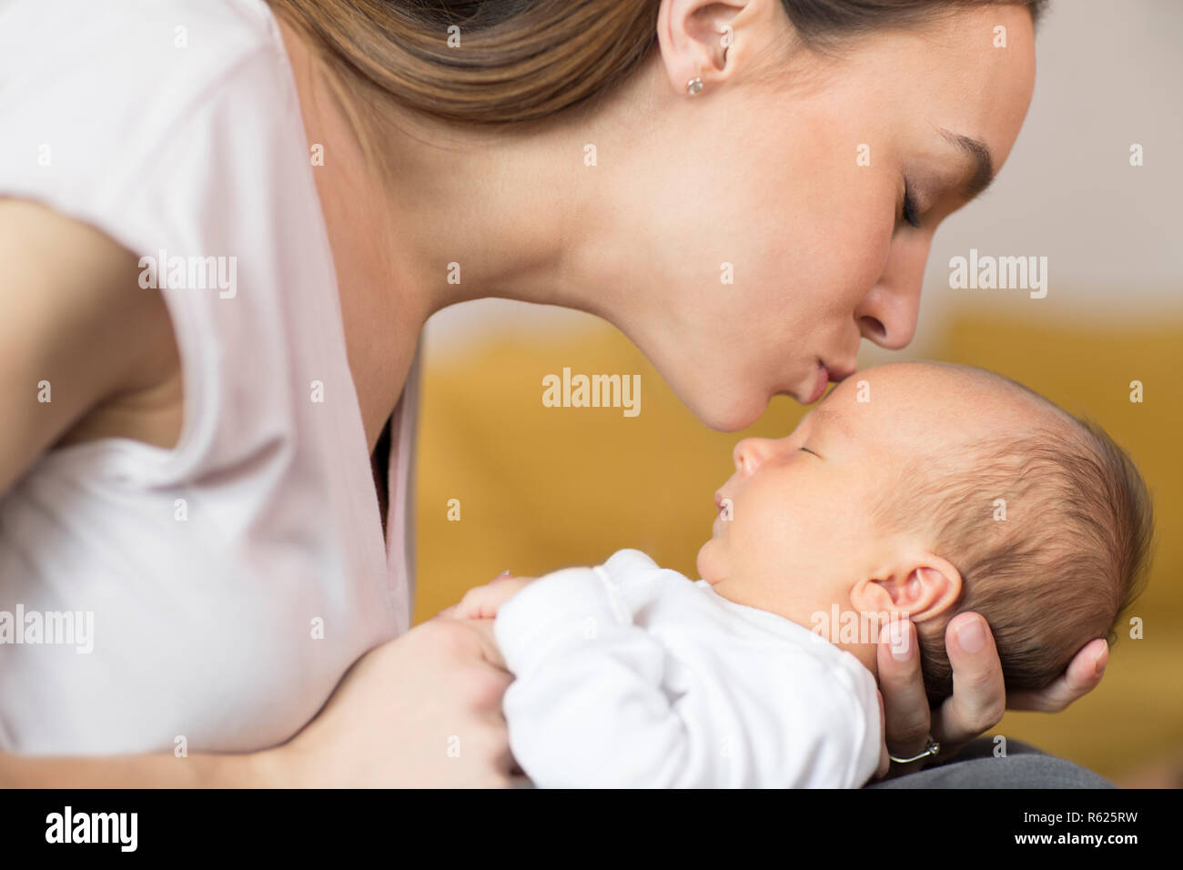 Liebevolle Mutter Kuscheln Baby Sohn und ihm auf die Stirn Küssen Stockfoto