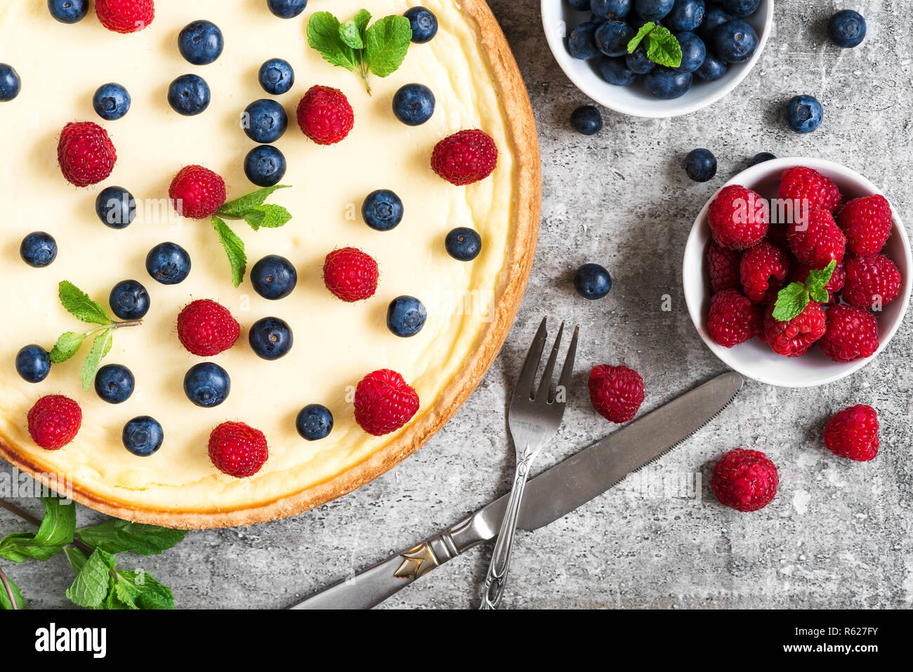 Classic New York Cheesecake mit frischen Beeren, Minze und Besteck auf Stein, Ansicht von oben. Leckeres Frühstück Stockfoto