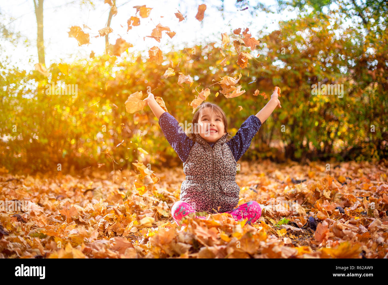 Kleine und schöne Mädchen genießen im Herbst und die Blätter werfen Stockfoto