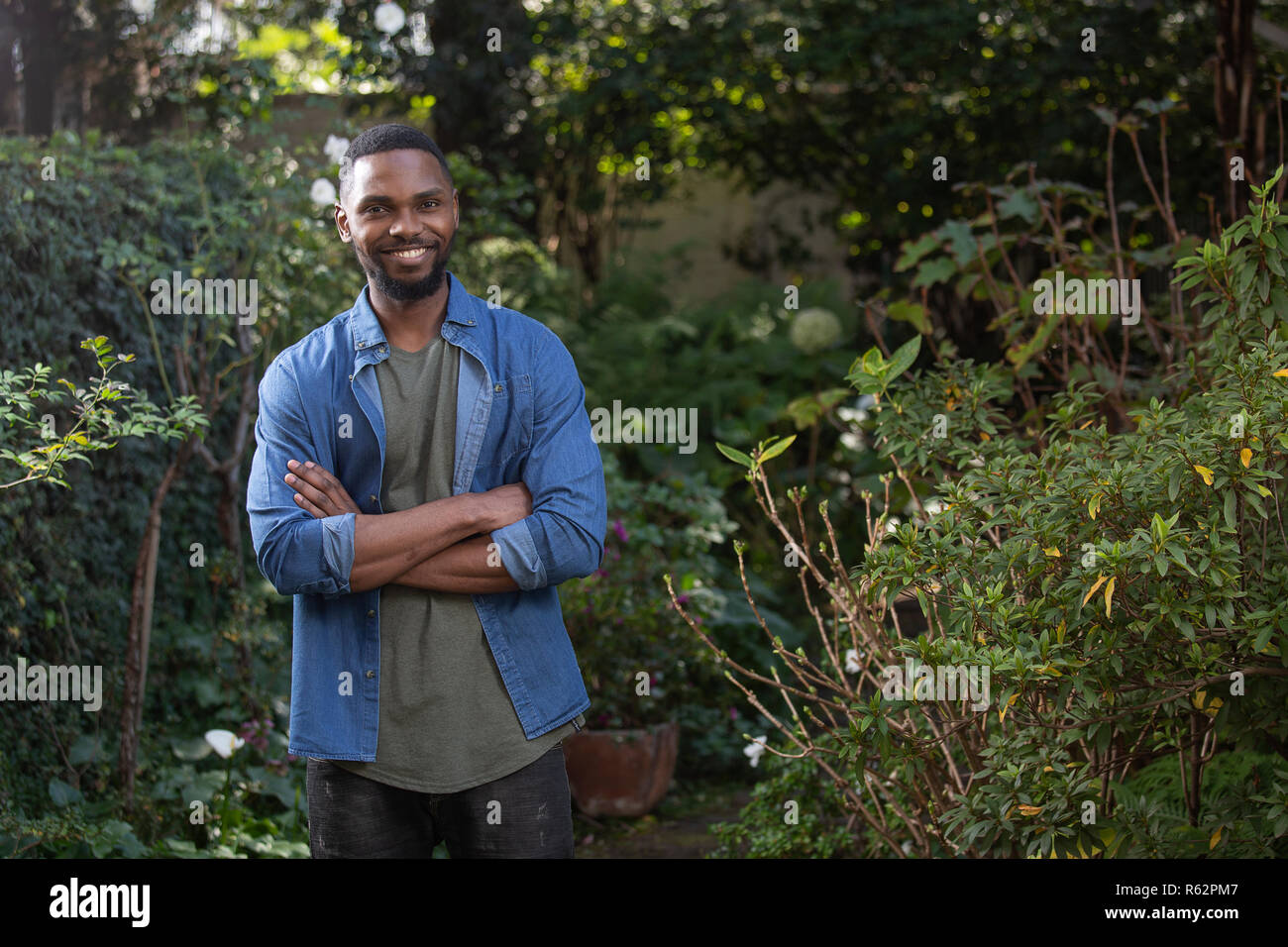 Ein afrikanischer Mann in einem Garten, Arme gekreuzt Stockfoto