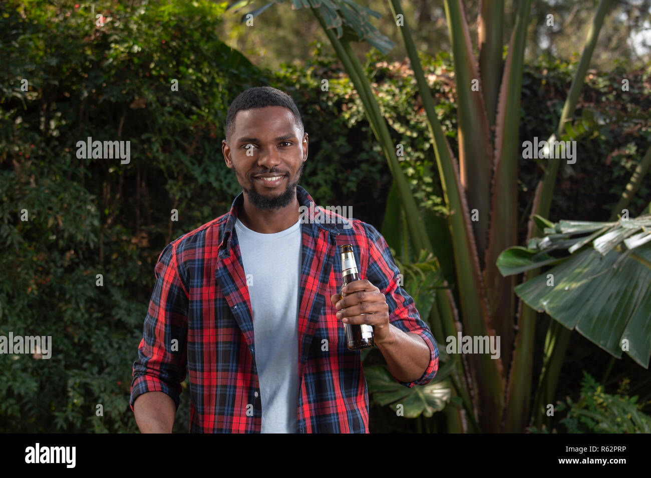 Ein afrikanischer Mann hält ein Bier in einem Garten Stockfoto