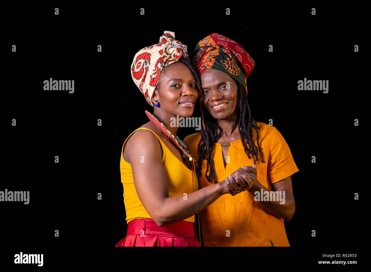 Eine afrikanische Mutter und Tochter halten sich an den Händen vor einem schwarzen Hintergrund Stockfoto