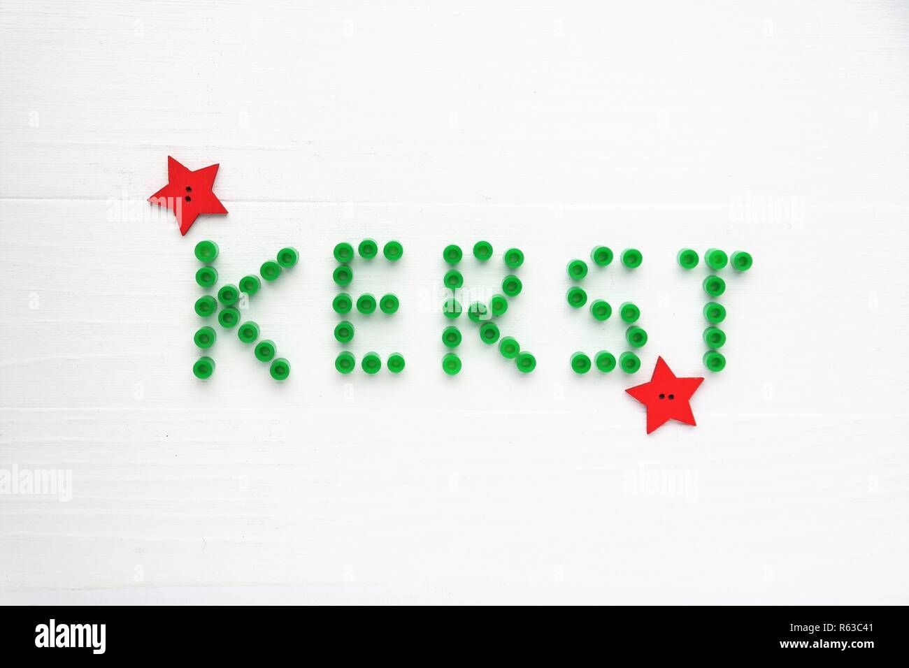 Weihnachtskarte in niederländischer Sprache. Dekorative grüne Buchstaben, perler Perlen und roten Sternen. Weiß Holz- Hintergrund. Draufsicht Perspektive und Text. Stockfoto