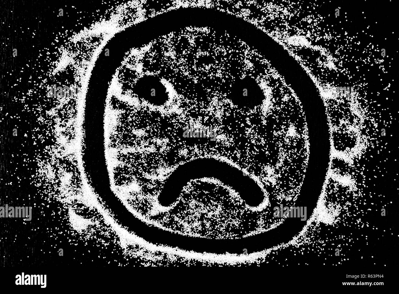 Symbol trauriges Lächeln emoticon Zeichnung mit dem Finger auf weißem Schnee Salz Pulver auf schwarzem Hintergrund. Konzept mit Platz für Text. Kopieren Sie Platz. Stockfoto