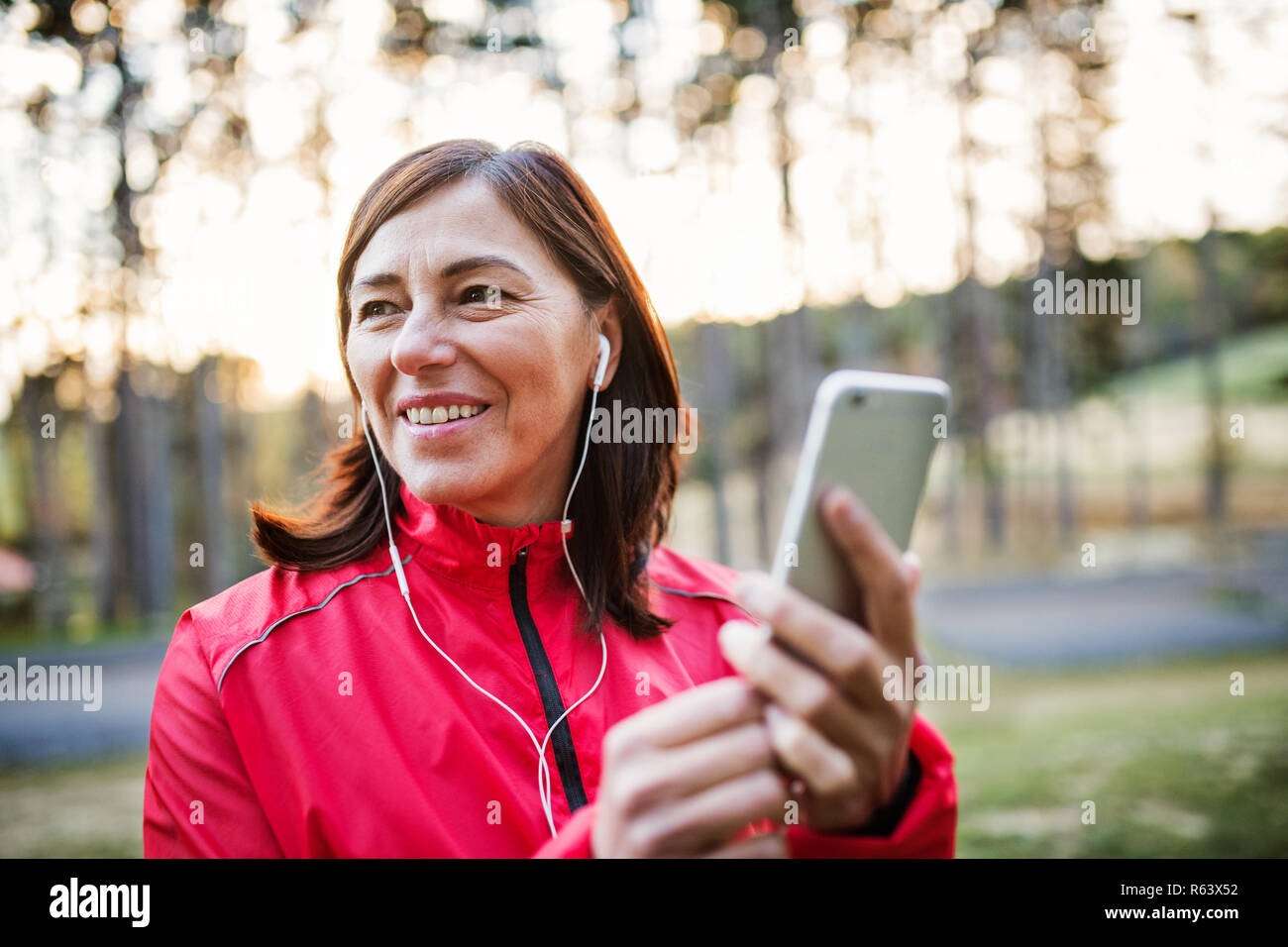 Eine Läuferin mit Ohrhörer im Freien im Herbst Natur, mit Smartphone. Stockfoto